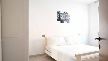 Ein Schlafzimmer mit einem Bett, weißen Wänden und einem kleinen Bild an der Wand.