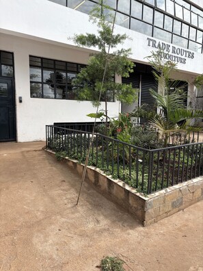 A building with a sign reading 'TRADE ROUTES FURNITURE' and a small garden area with a metal fence. - 2-bedroom in secure leafy area Conveniently close to a coffee shop & restaurants (Nairobi)
