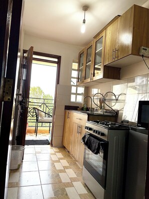 A kitchen with wooden cabinets, a stove, and a refrigerator. - 2-bedroom in secure leafy area Conveniently close to a coffee shop & restaurants (Nairobi)