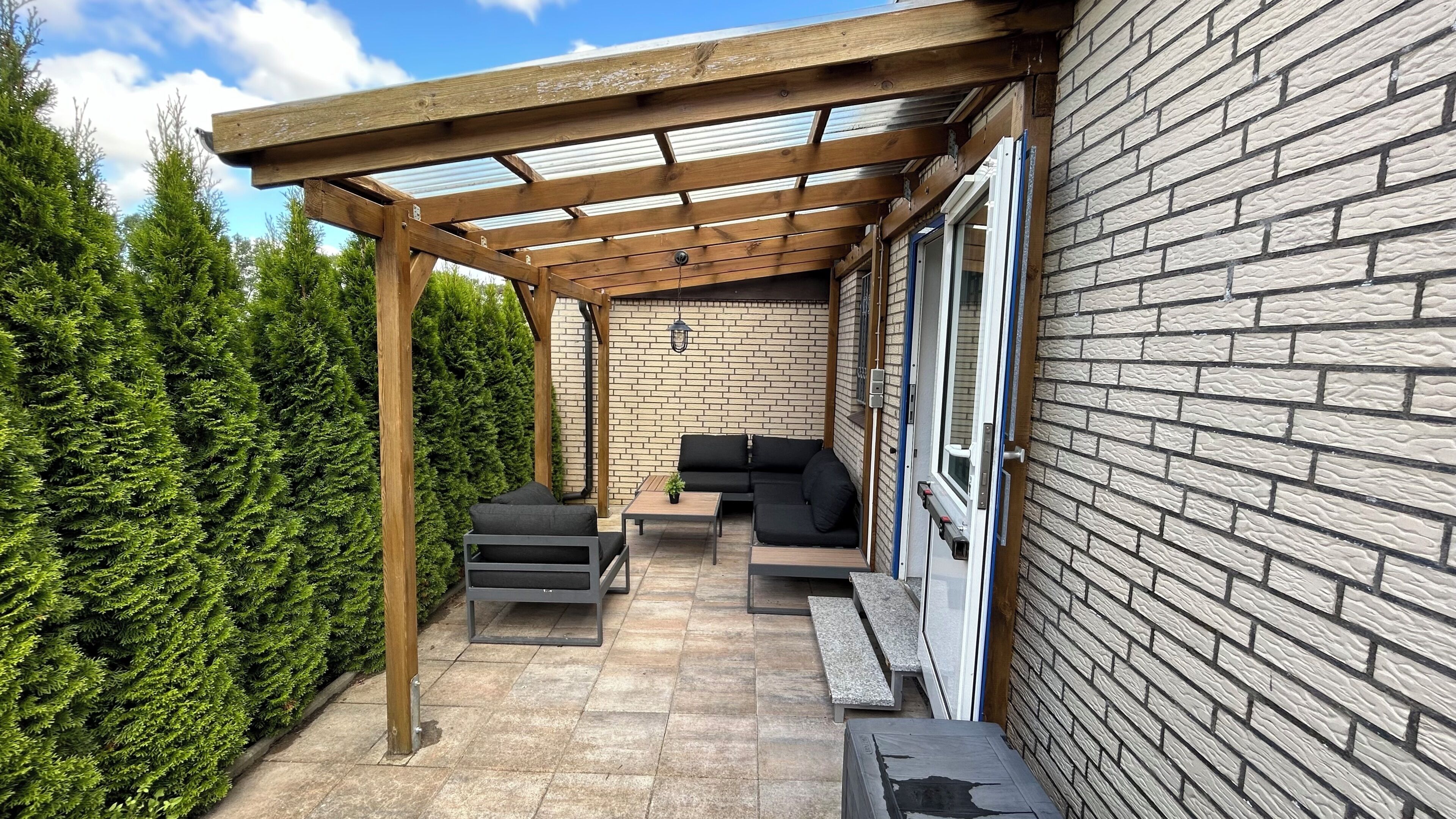 Un patio couvert avec un mur en briques, une pergola en bois et du mobilier d’extérieur.