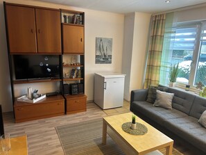 A living room with a flat-screen TV, wooden cabinets, a small fridge, a sofa, and a coffee table. - Dino House in a quiet location—1 km from the dike in Stinteck and 8 km from Büsum (Westerdeichstrich)