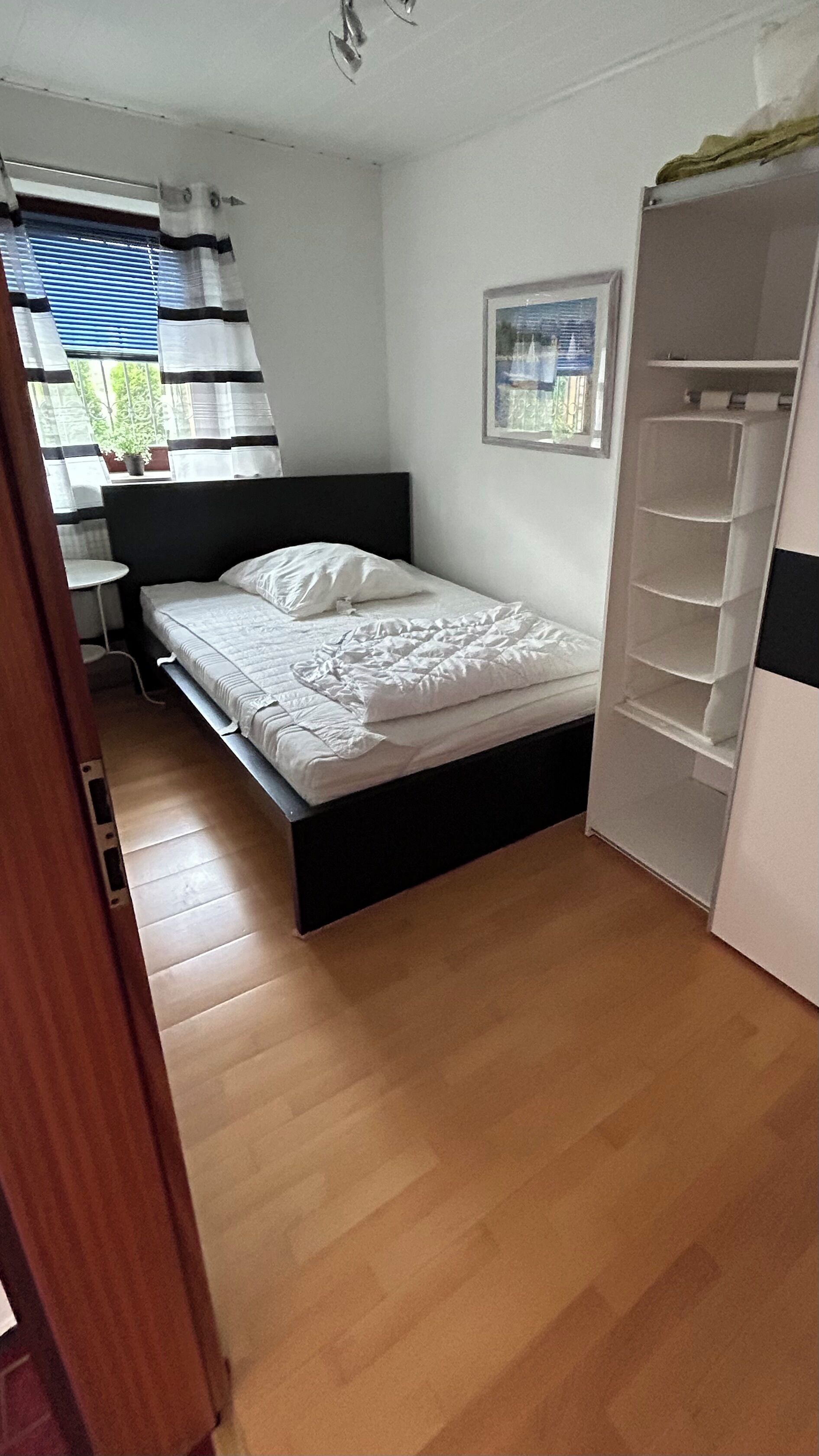A bedroom with a bed, a wardrobe, and a window with blinds.