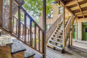 Eine Holzterrasse mit einer Treppe zu einer grünen Tür, einem Holztisch und Blick auf ein Backsteingebäude.