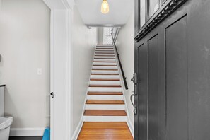 Eine Treppe mit weißen Wänden und Holzstufen, die zu einer dunklen Tür führt.