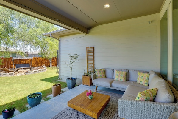 A covered patio with a sofa, coffee table, and potted plants.