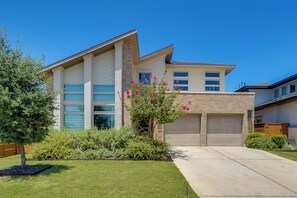 A two-story residential building with a garage, a well-maintained lawn, and flowering shrubs. - Easy Airport & I-35 Access: Modern Austin Home (Austin)