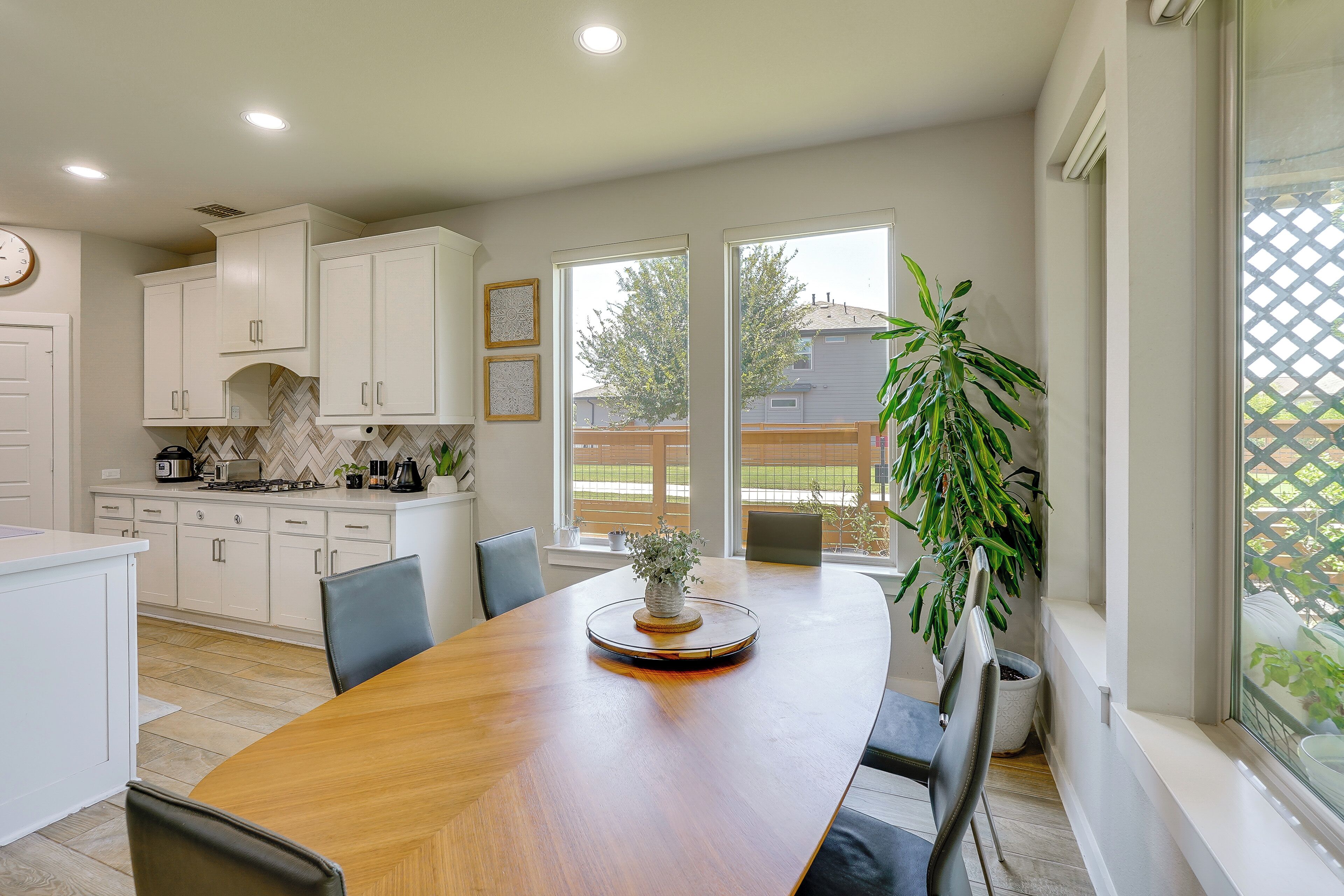 A modern kitchen with white cabinets, a wooden dining table, and a large window with a view of the outdoors.