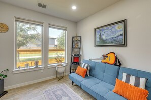 A living room with a blue sofa, a guitar, a framed painting, and a Buddha statue. - Easy Airport & I-35 Access: Modern Austin Home (Austin)
