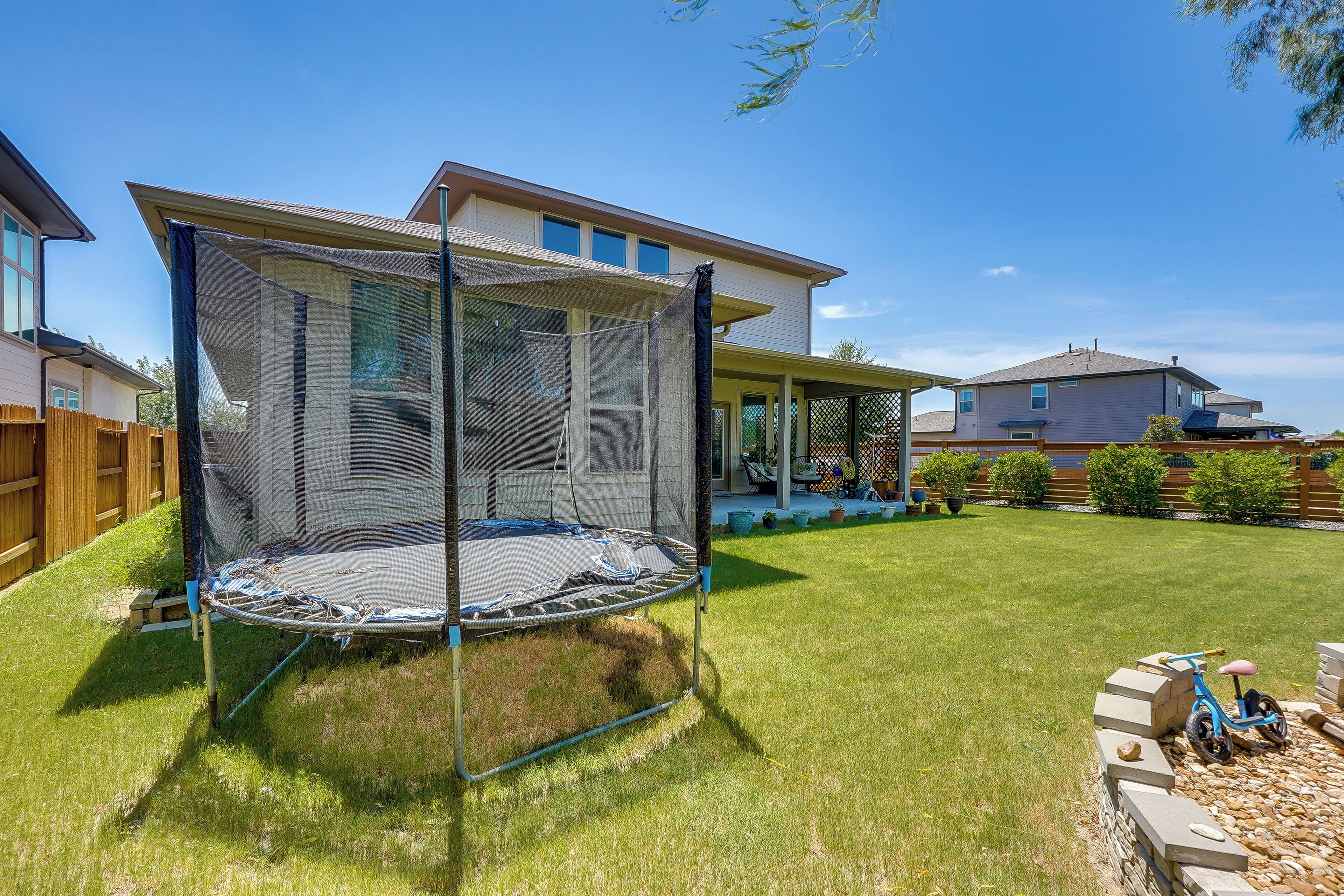 A residential backyard with a trampoline, a wooden fence, and a house with a porch.