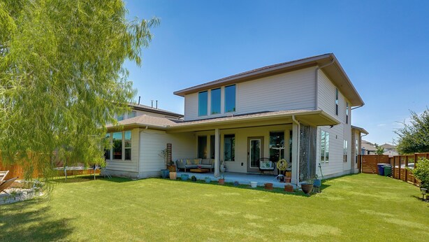 Ein zweigeschossiges Haus mit einer Veranda, einem Rasen und einem großen Baum.
