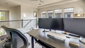 Ein moderner Arbeitsbereich mit einem großen Schreibtisch, einem Computermonitor und einem Stuhl. Eine Treppe mit Geländer führt zu einer erhöhten Ebene.