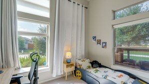 Ein Kinderzimmer mit Bett, Schreibtisch und einem fenster mit Vorhängen.