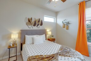 A bedroom with a bed, bedside lamps, a ceiling fan, a window with curtains, and wall art. - Easy Airport & I-35 Access: Modern Austin Home (Austin)