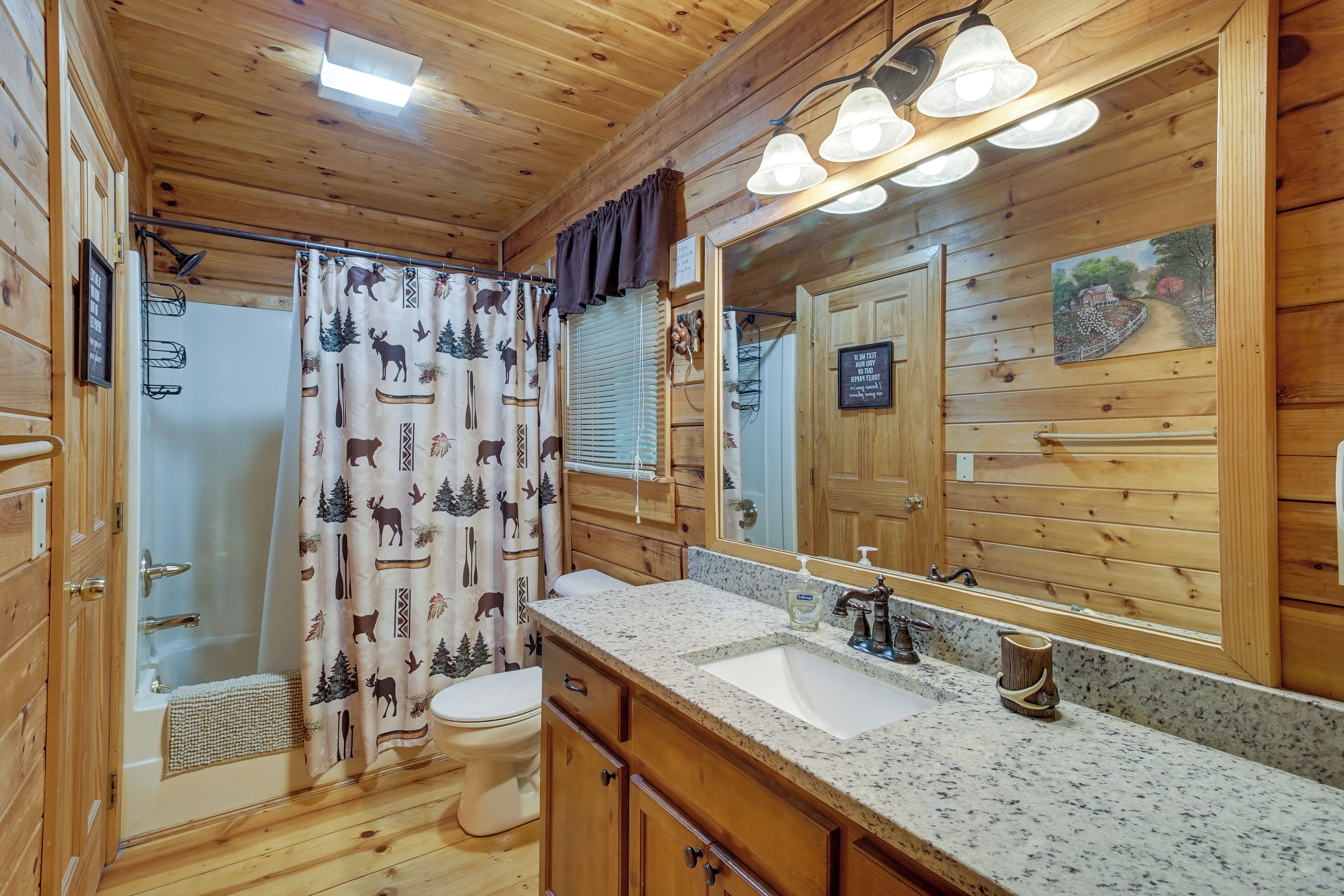 A wooden cabin bathroom with a shower curtain, toilet, sink, and a large mirror.
