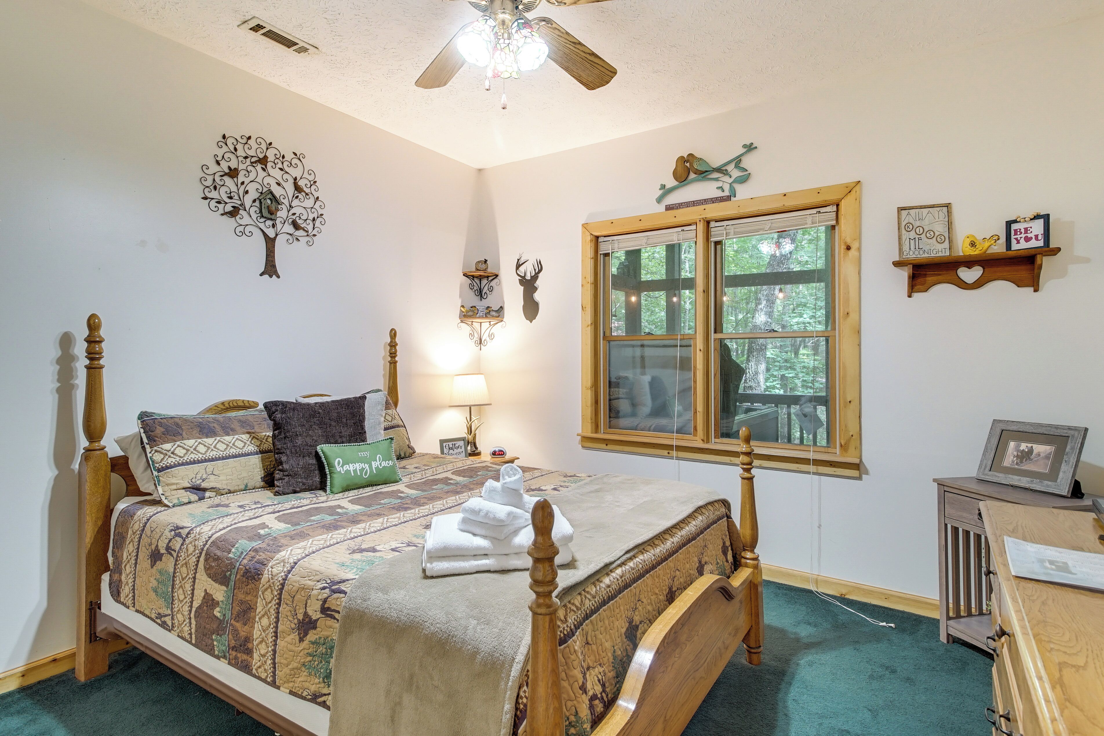 A bedroom with a wooden bed, a window with a view, a ceiling fan, and wall decorations.