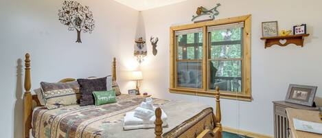 A bedroom with a wooden bed, a window with a view, a ceiling fan, and wall decorations.