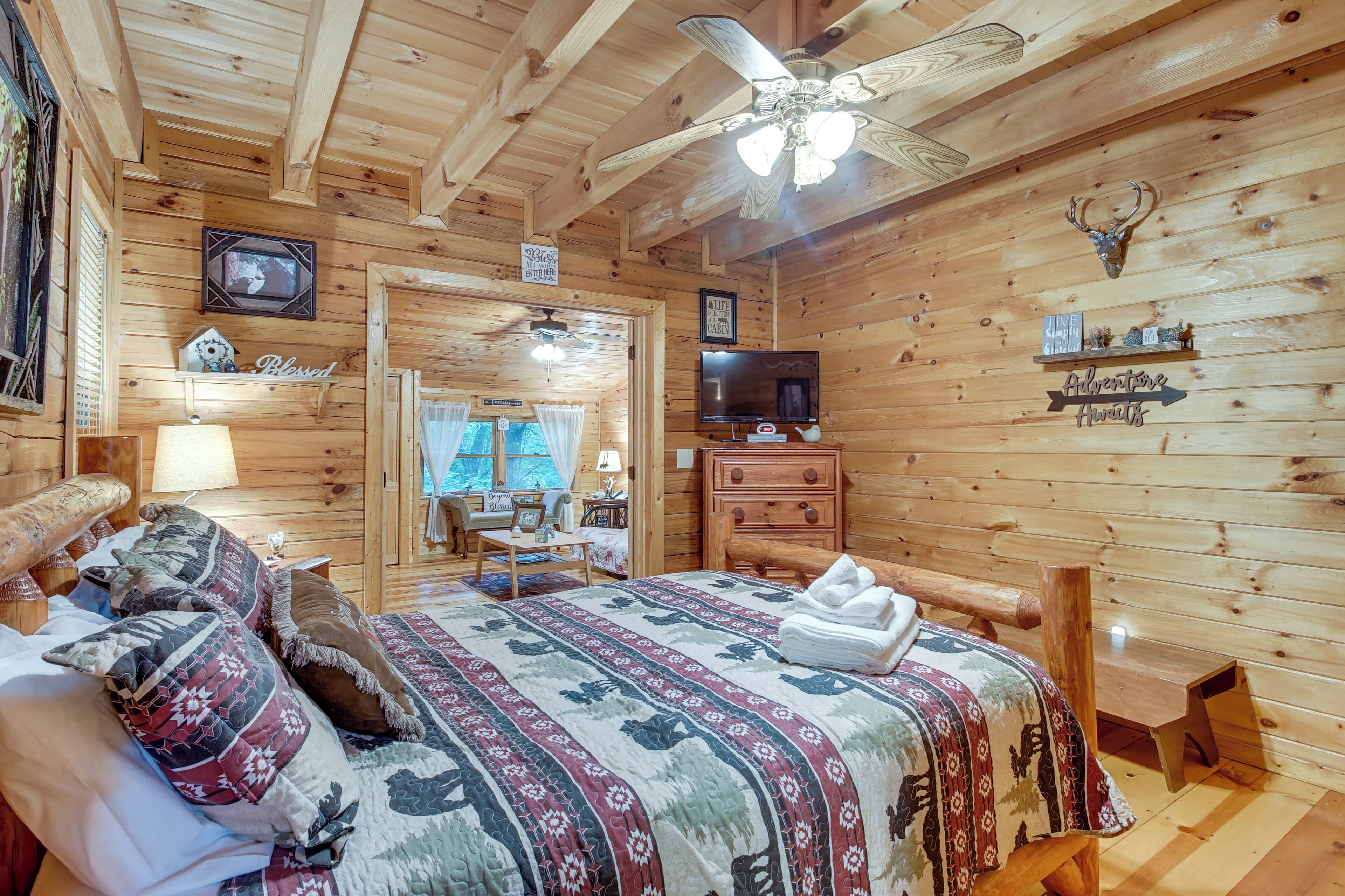 A wooden cabin bedroom with a bed, a television, a ceiling fan, and a sign indicating a 'Blessed' room.