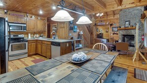 A wooden cabin interior with a kitchen, dining area, and fireplace. - Hot Tub & Game Room! Wooded Retreat in Blue Ridge (Blue Ridge)