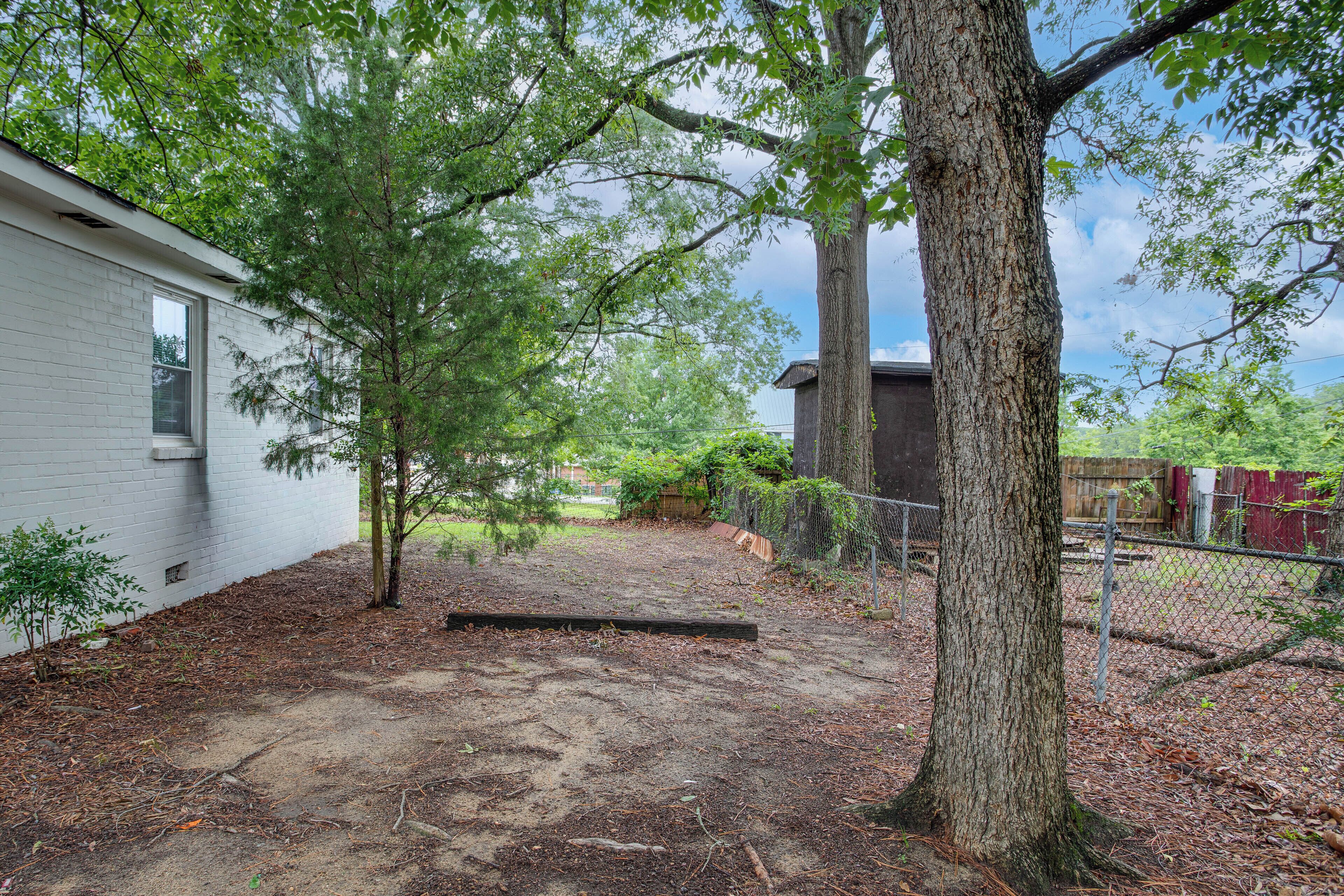 A fenced backyard with a white building, a tree, and a wooden bench.