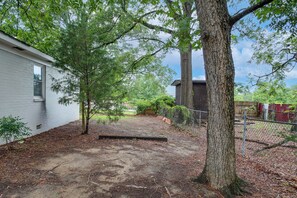 A fenced backyard with a white building, a tree, and a wooden bench.