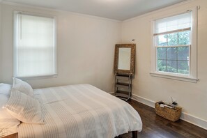 Een slaapkamer met een bed, twee ramen, een spiegel en een klein plankje.