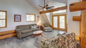A spacious living room with a high ceiling, wooden beams, a ceiling fan, and large windows. - Real Log Cabin in Flagstaff With Forest Views (Flagstaff)
