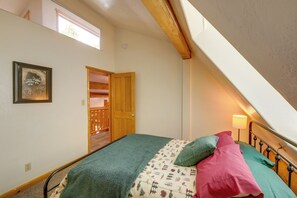 A bedroom with a sloped ceiling, a bed with patterned bedding, a bedside lamp, and a framed picture on the wall. - Real Log Cabin in Flagstaff With Forest Views (Flagstaff)
