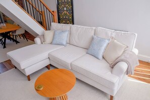 A white sectional sofa with a chaise, two patterned pillows, a small wooden coffee table, and a staircase in the background. - Relax at Pebble House for a seaside break. (Whitstable)