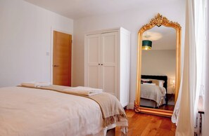 A bedroom with a bed, a wardrobe, a mirror, and a door. - Relax at Pebble House for a seaside break. (Whitstable)