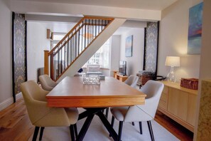 A dining area with a wooden table, four chairs, a staircase, and a view of the city. - Relax at Pebble House for a seaside break. (Whitstable)