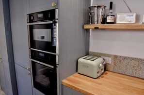 A kitchen with a built-in oven, a toaster, and a radio on a shelf. - Relax at Pebble House for a seaside break. (Whitstable)