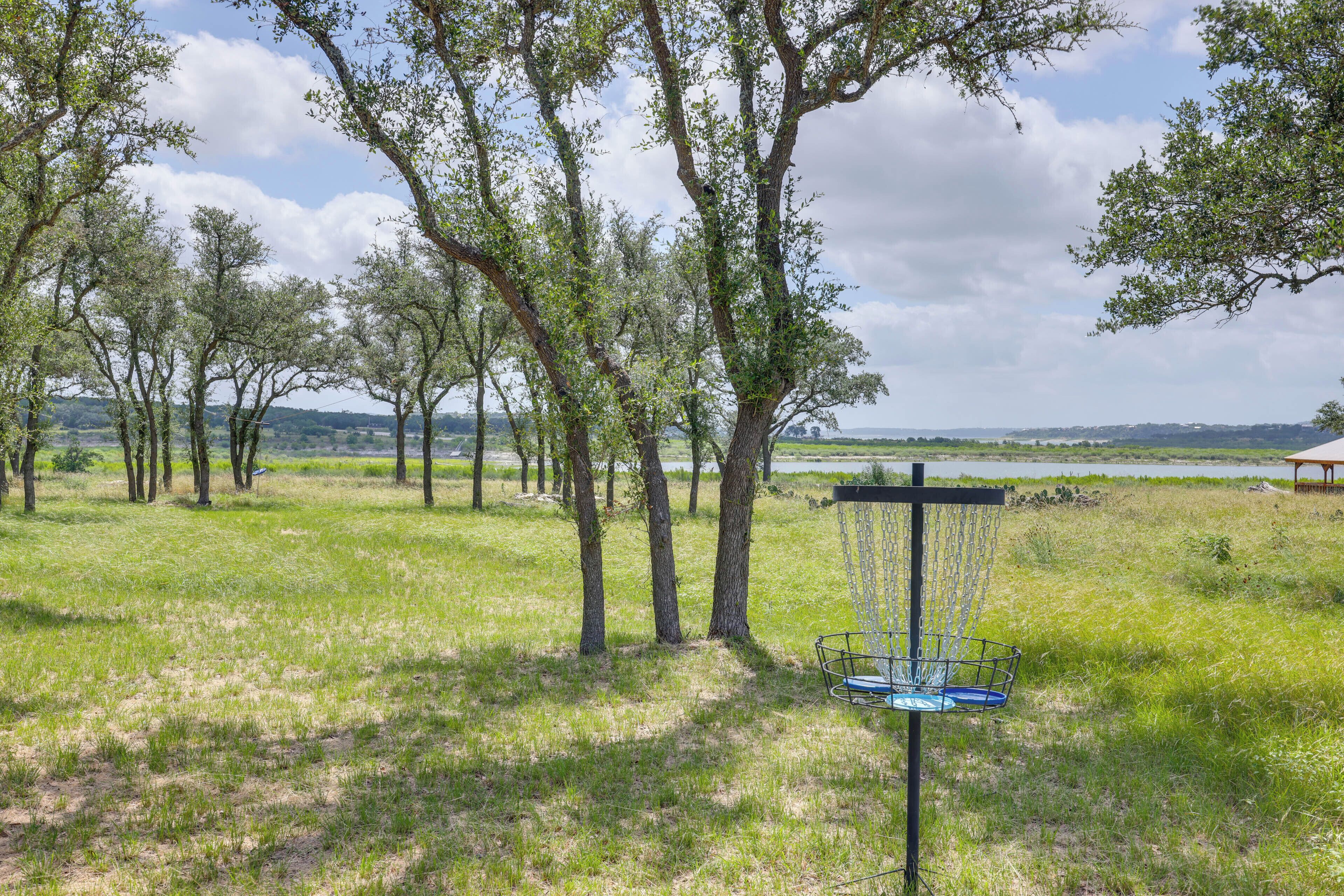 Ein Außenbereich mit einem Disc Golf Korb, Bäumen und Blick auf einen See.