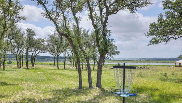 An outdoor area with a disc golf basket, trees, and a view of a lake. - Walk to Shore! Family-friendly Canyon Lake Retreat (Canyon Lake)