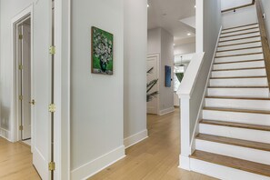 Ein Flur mit einer Holztreppe, einer Tür mit Riegel und einem Gemälde an der Wand.