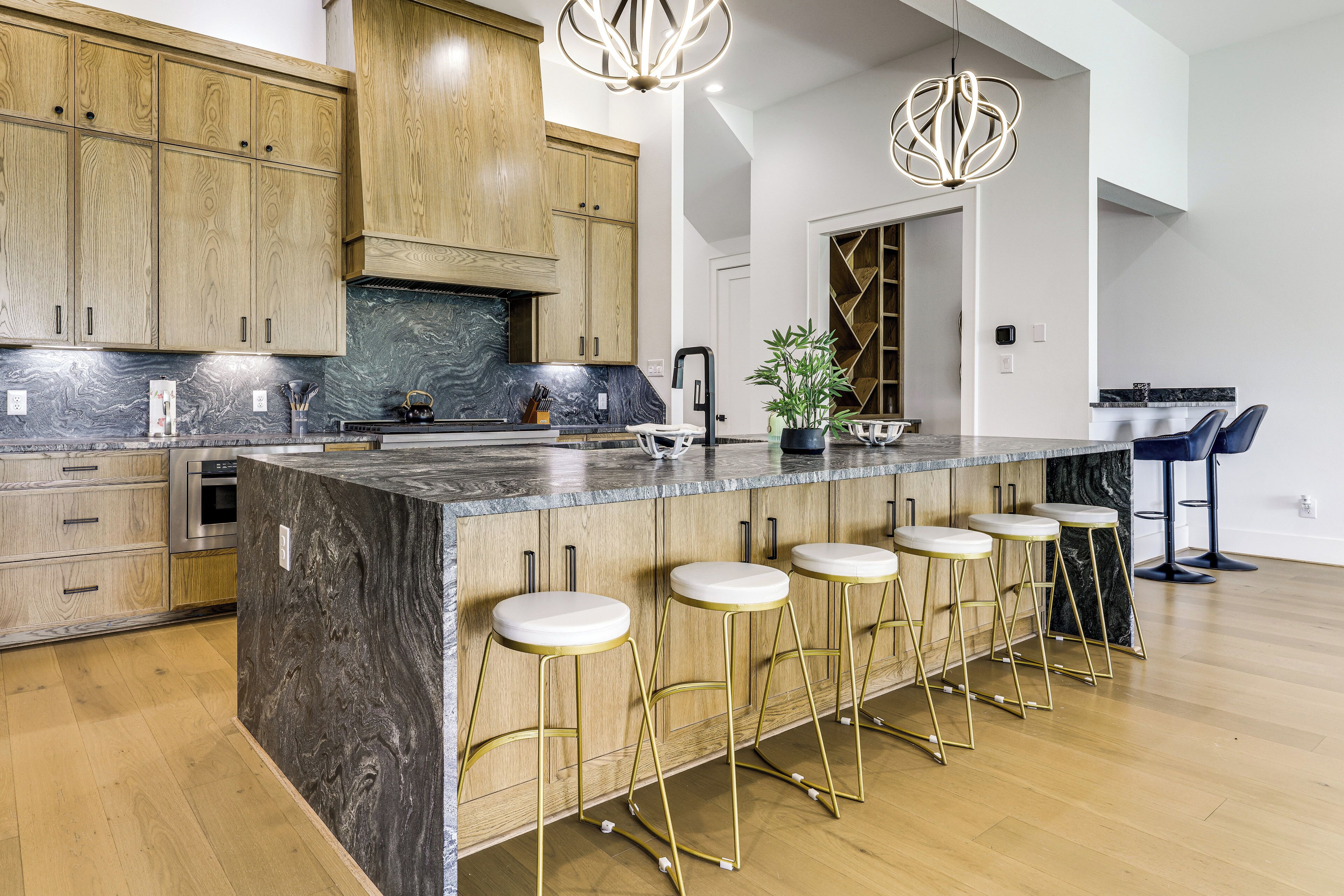 A modern kitchen with wooden cabinets, a marble island, bar stools, and pendant lighting.