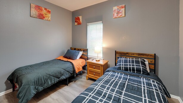 A bedroom with two single beds, a nightstand, a window with blinds, and two wall-mounted paintings. - Fenced Yard! Spacious Home, 4 Mi to Dtwn Milwaukee (Milwaukee)