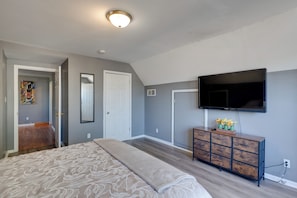 A bedroom with a bed, dresser, television, and artwork on the wall.