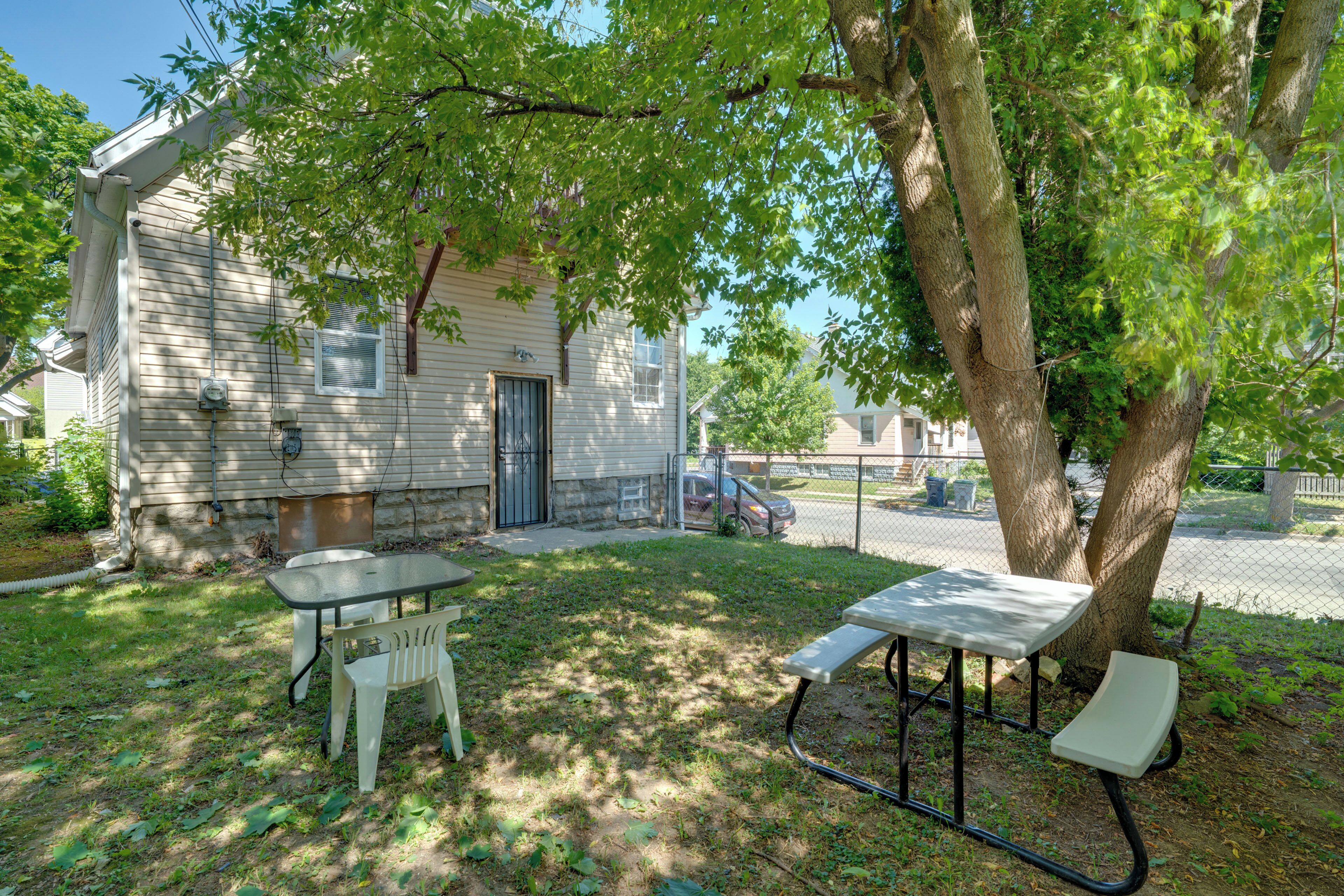 A residential property with a detached house, a paved driveway, and a fenced yard with picnic tables.