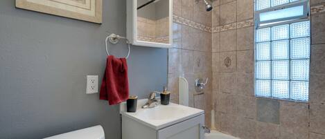 A bathroom with a toilet, sink, mirror, and shower.
