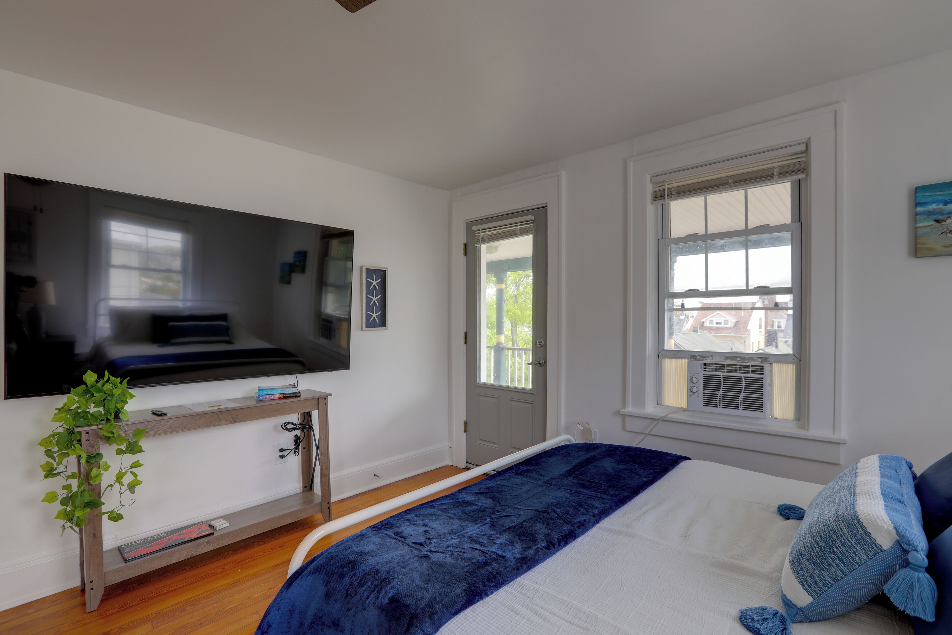 A bedroom with a bed, a TV mounted on the wall, a window, and a door.