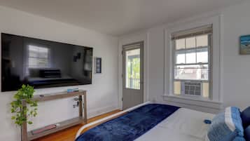 A bedroom with a bed, a TV mounted on the wall, a window, and a door.
