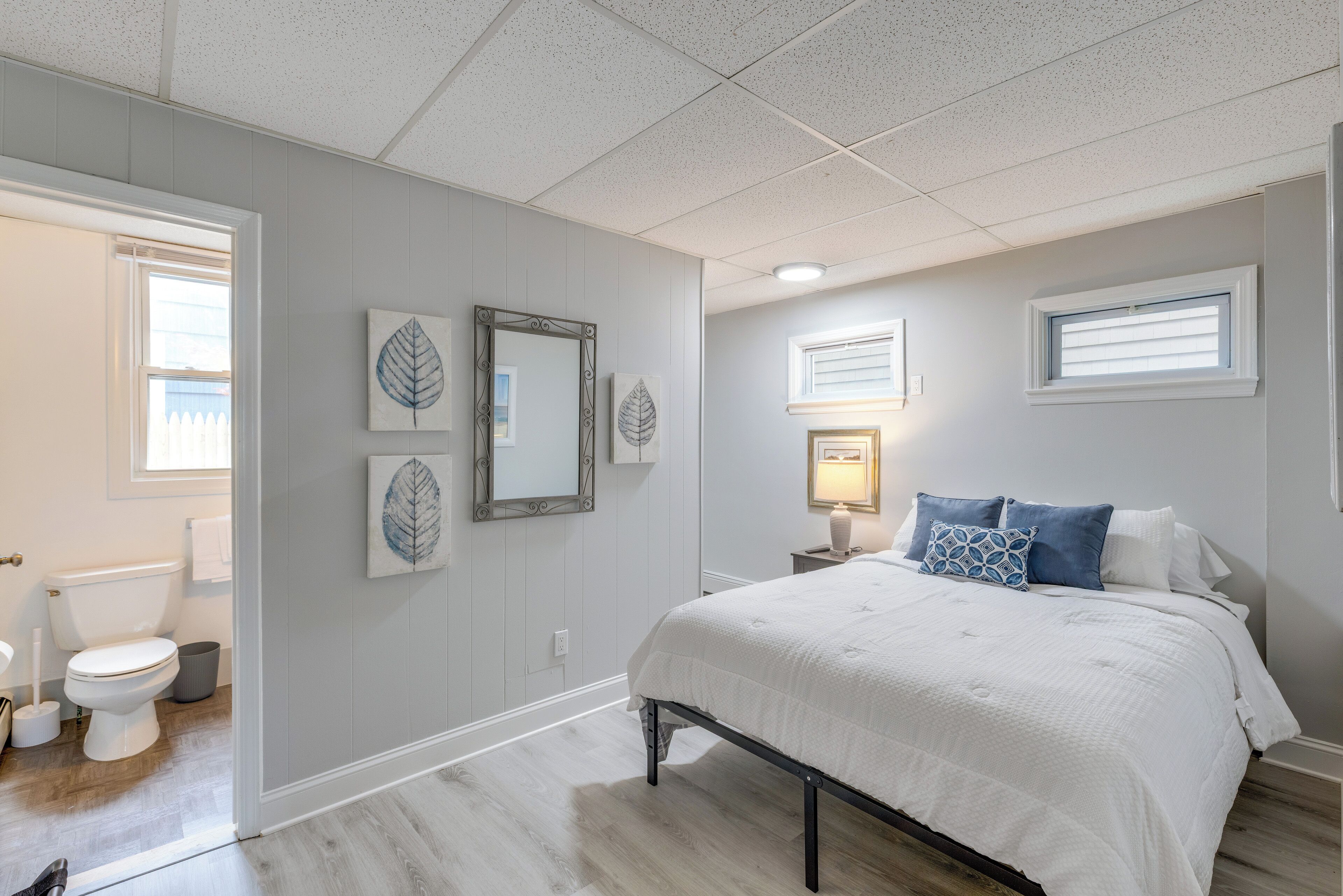 A bedroom with a bed, a nightstand, a wall-mounted lamp, and a window with blinds.