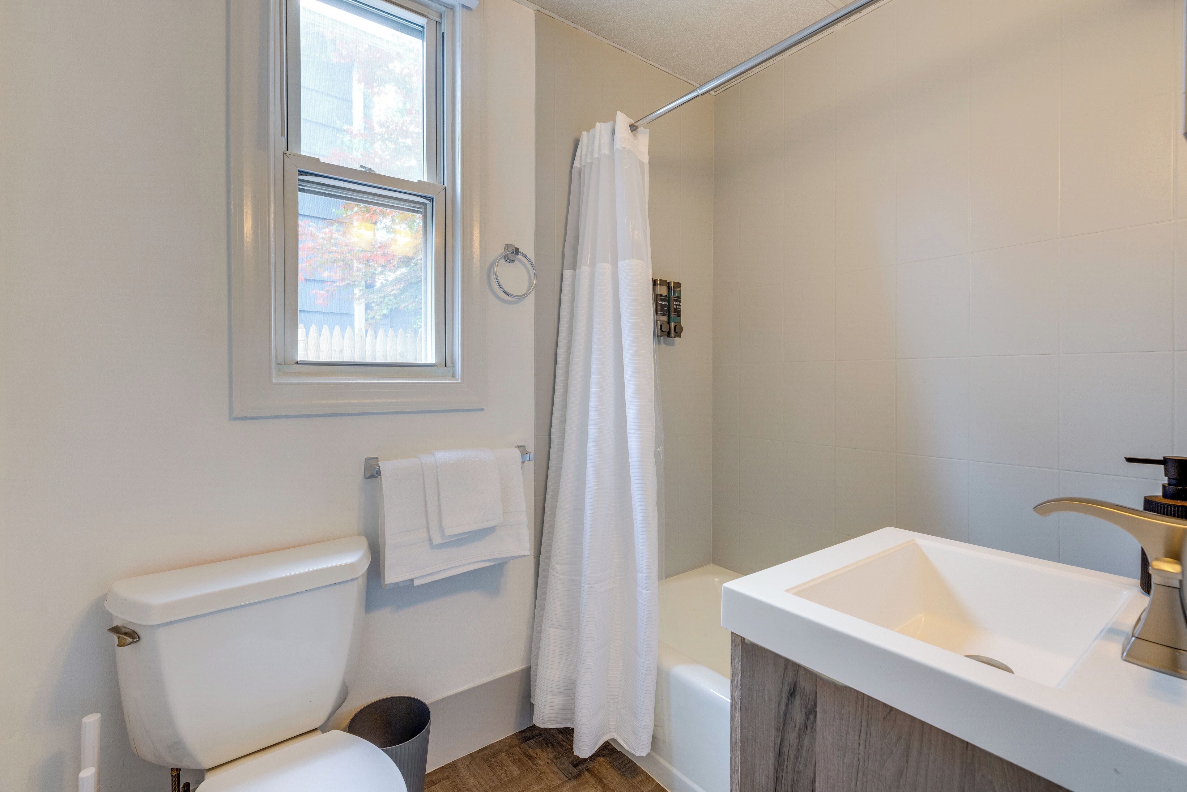 Un bagno con un water, una vasca, una finestra e una tenda da doccia.
