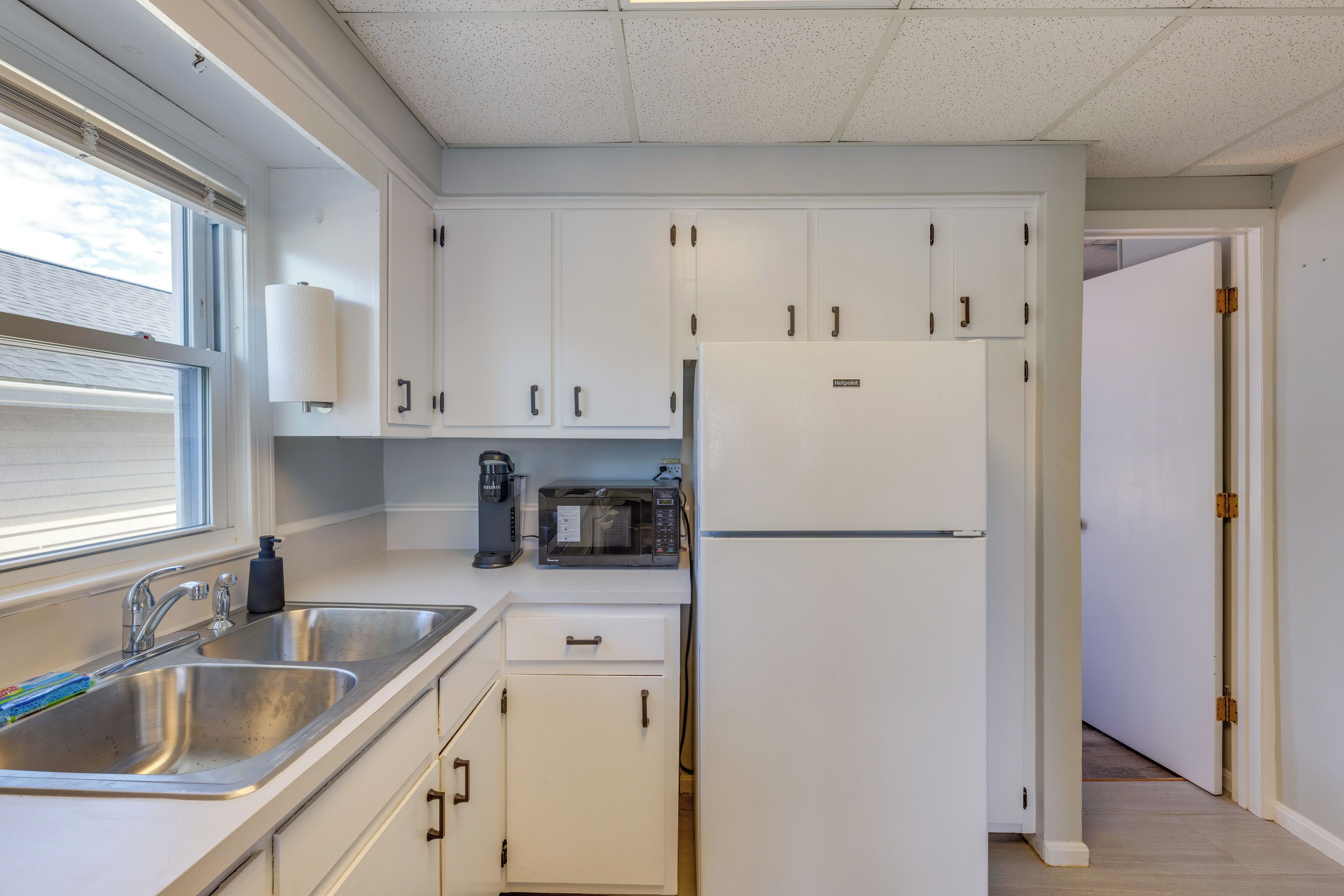 Una cocina con gabinetes blancos, un lavamanos de acero inoxidable, un microondas y un refrigerador.