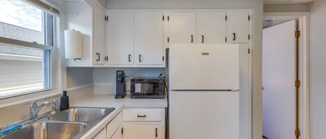 Una cocina con gabinetes blancos, un lavamanos de acero inoxidable, un microondas y un refrigerador.