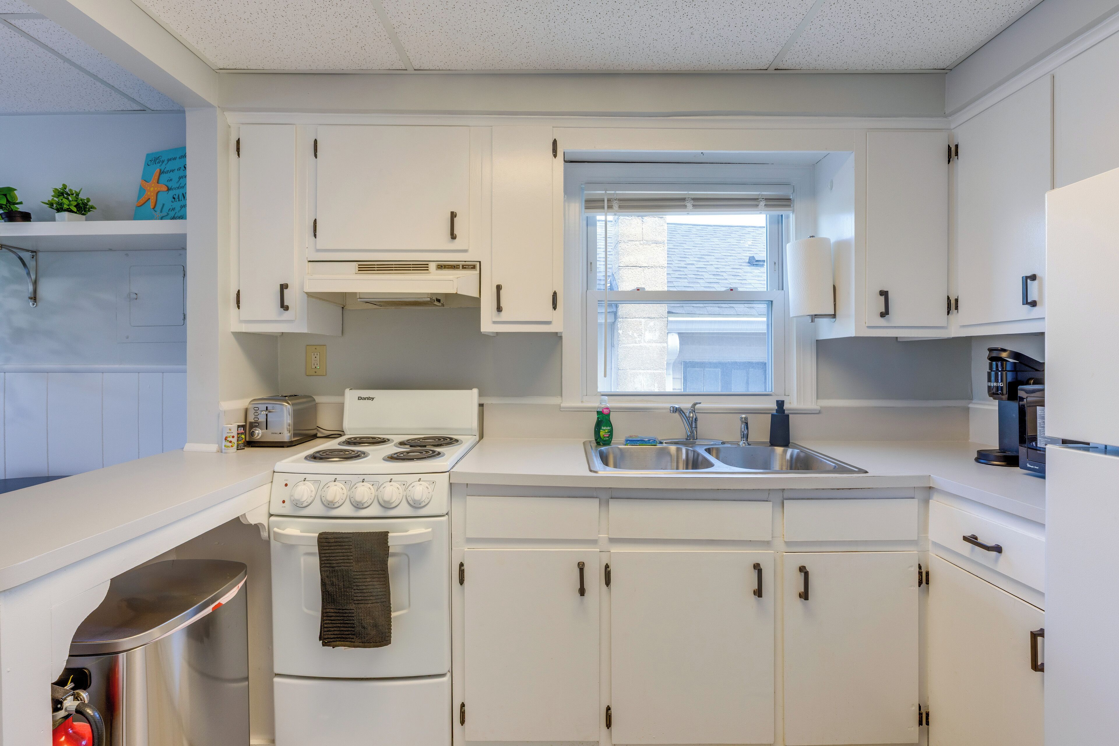 A kitchen with white cabinets, a stove, a sink, and a window.