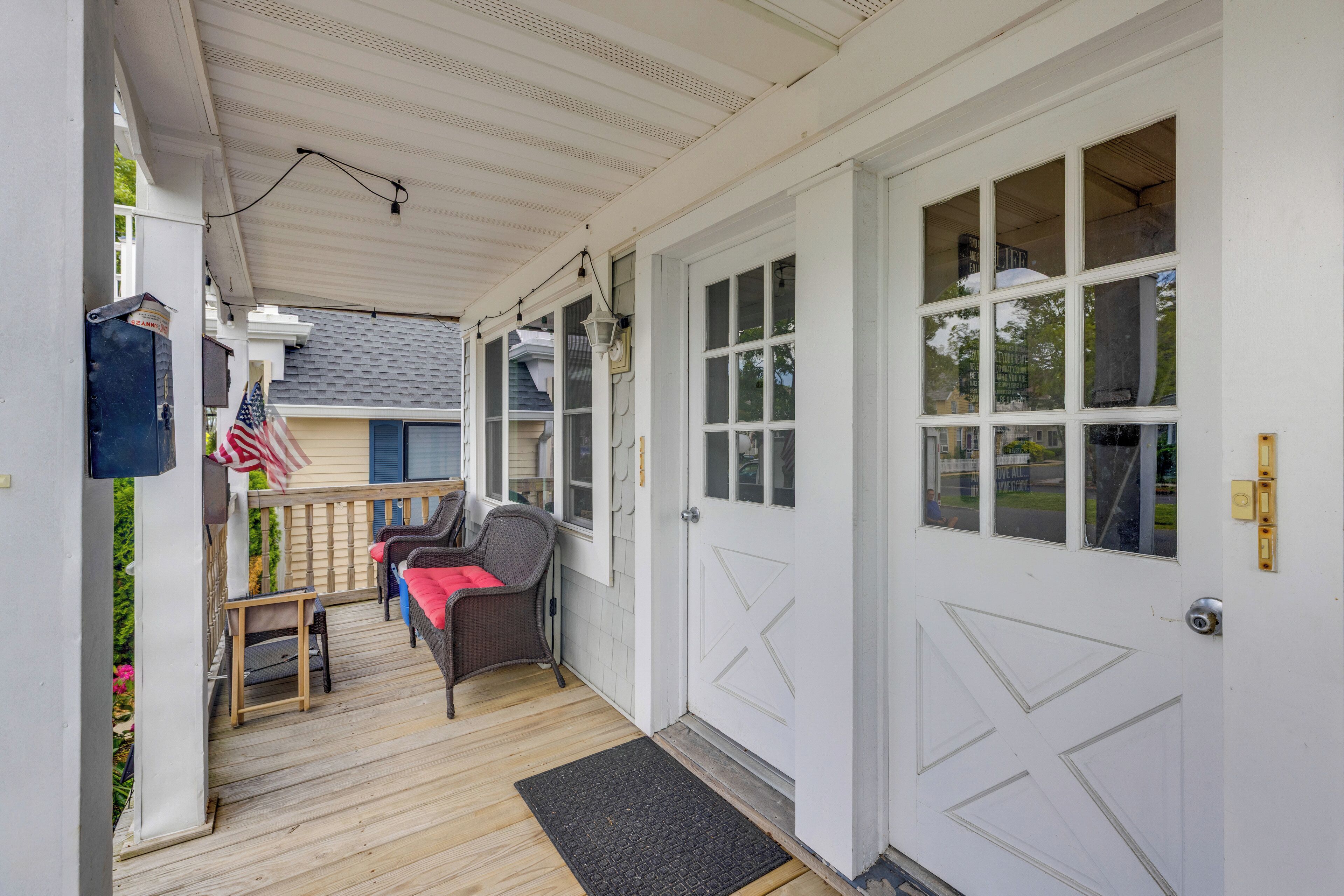 A covered porch with a wooden floor, a small table, two chairs, and an American flag.