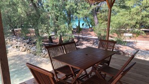 A wooden deck with a table and chairs, overlooking a natural landscape with trees and a body of water. - Desa Laguna Regenerative Village Resort (Karang Bongkok Island)