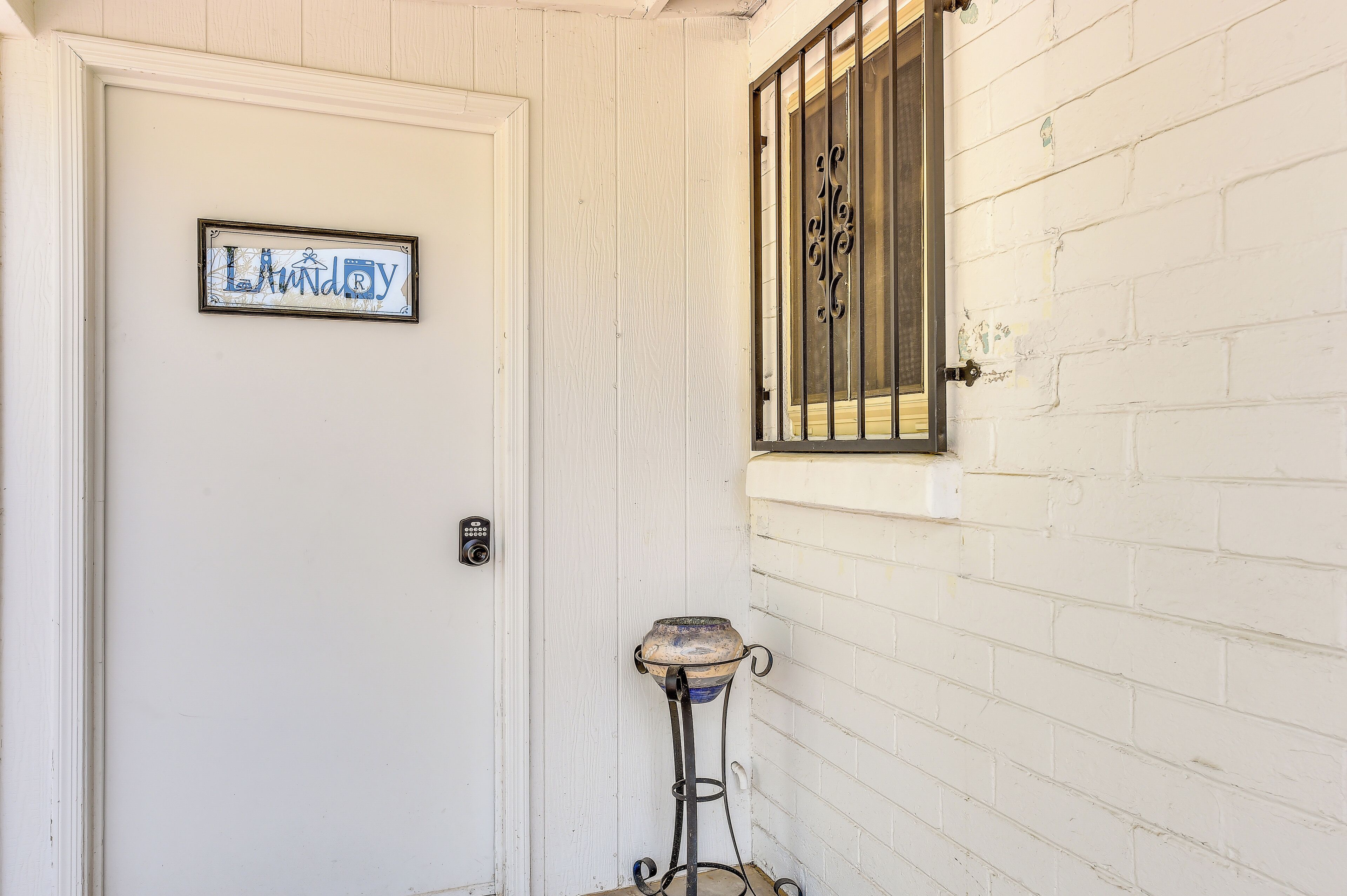 A white door with a sign that reads 'Laundry' and a metal gate on a white brick wall.