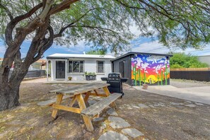 Ein kleines Haus mit Terrasse, Grill und einer farbenfrohen Wandmalerei.